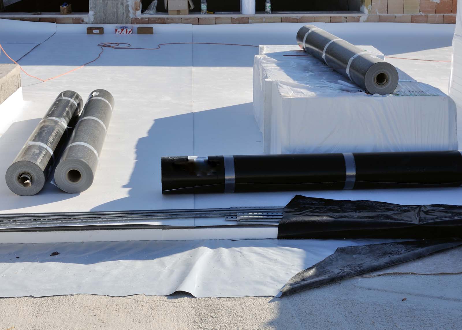 Rolled materials, possibly roofing or insulation, are placed on a flat white surface at a construction site.